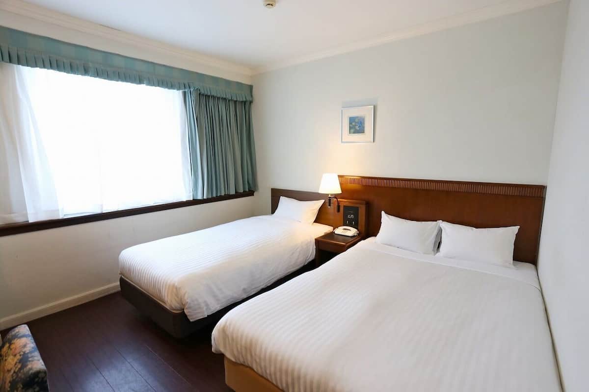 Quarto de hotel com duas camas de solteiro, mesa de cabeceira com abajur, telefone e um quadro na parede.