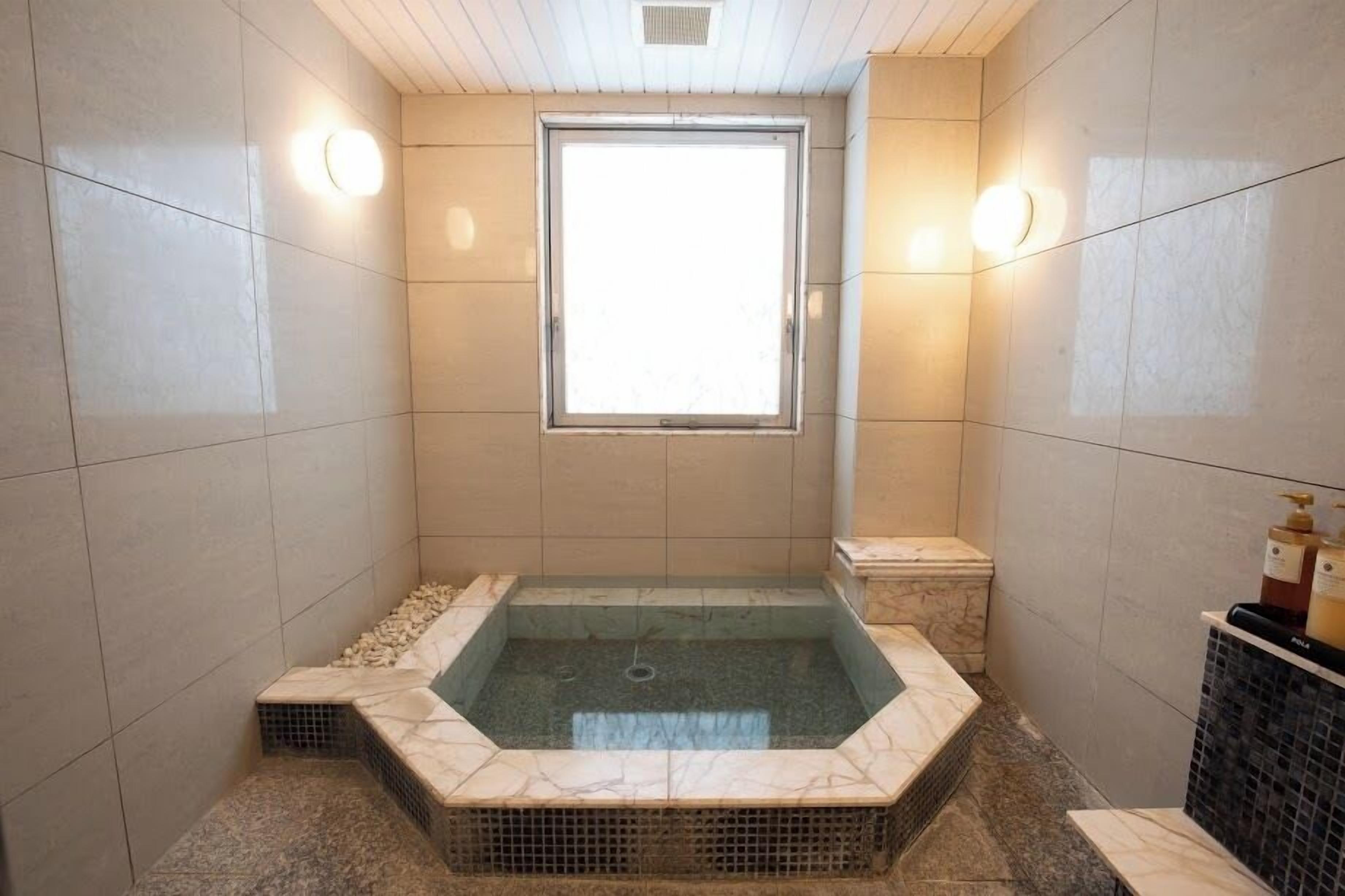 A modern bathroom with a freestanding bathtub, a window, and a tiled floor.