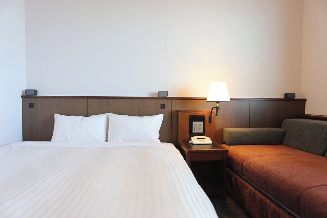 Une chambre d’hôtel avec un lit, une table de chevet avec une lampe et un petit bureau avec un téléphone.