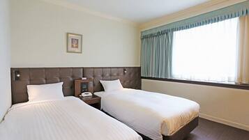 A hotel room with two beds, a headboard, a bedside table with a phone, and a window with curtains.