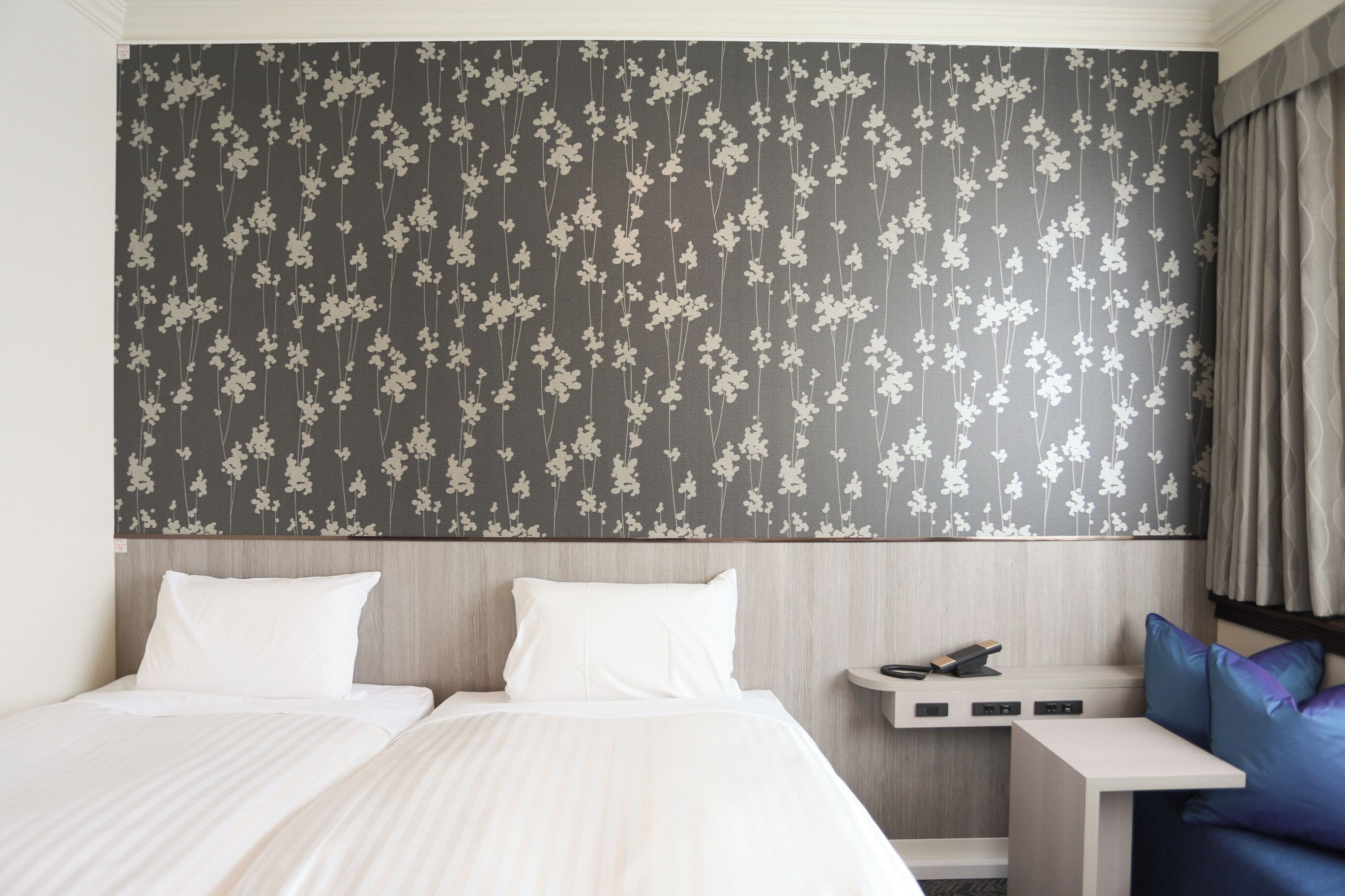 A hotel room with a large bed, a desk with a phone, and a seating area with cushions.
