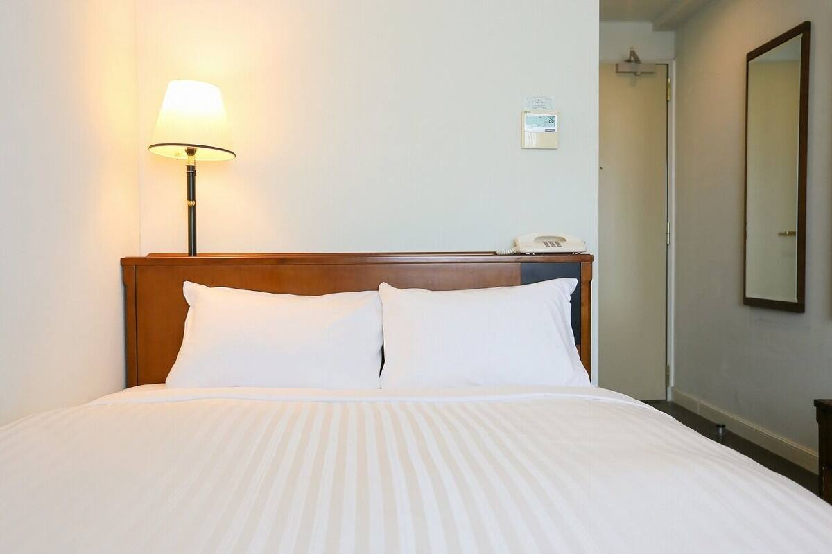 Quarto de hotel com cama, abajur, telefone e espelho na parede.