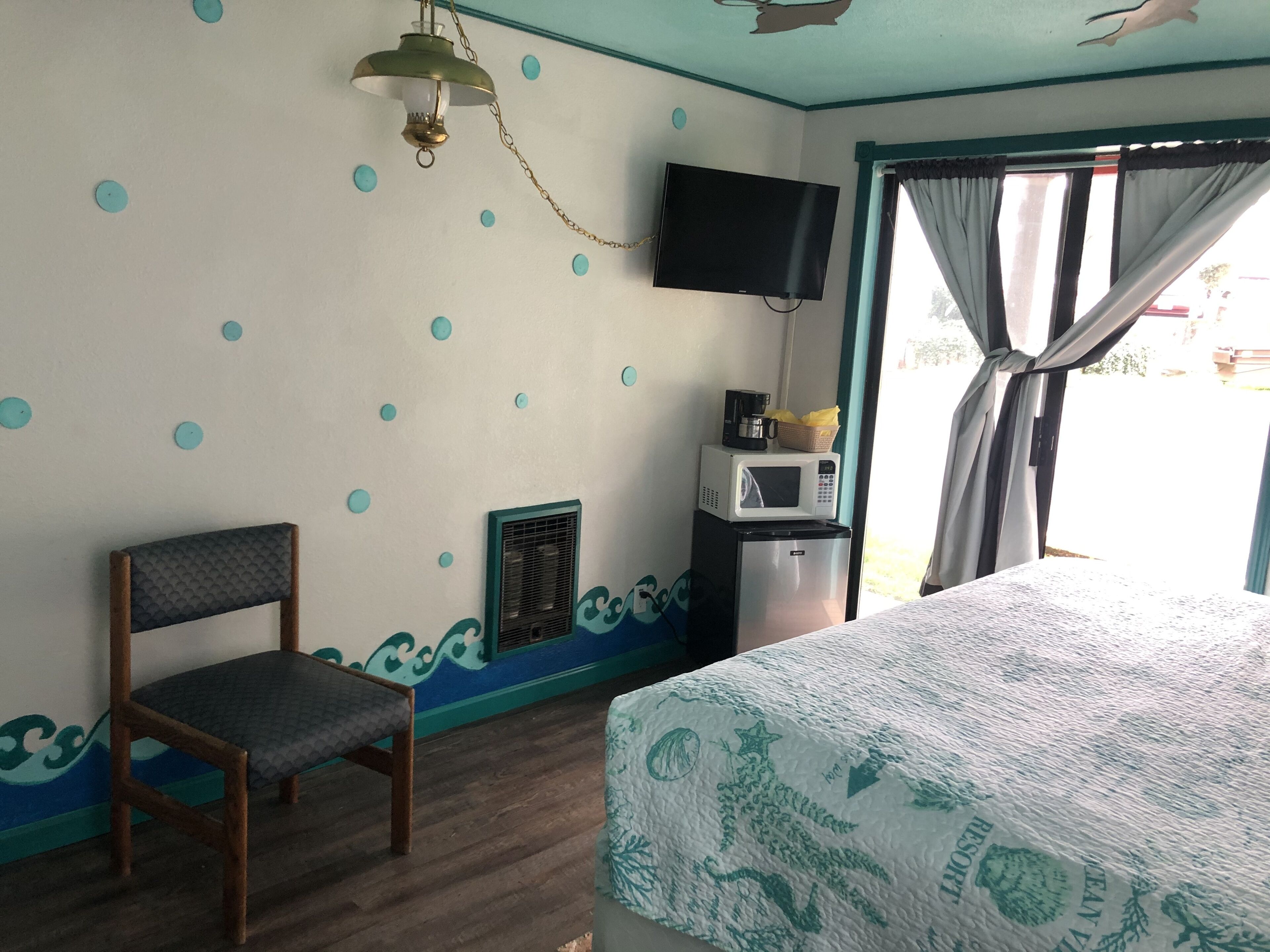 Een kamer met een bed, een stoel, een televisie, een magnetron en een raam met gordijnen.