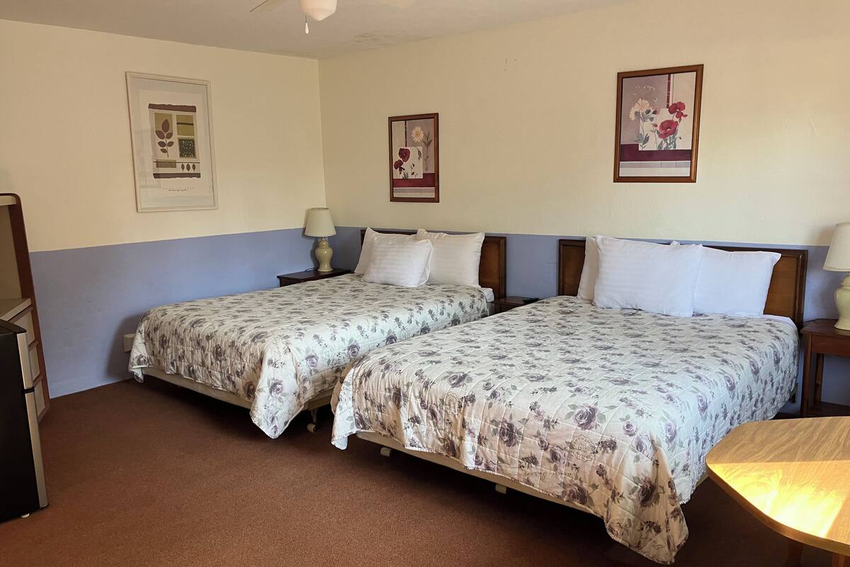A room with two single beds, a small table, and a ceiling fan.