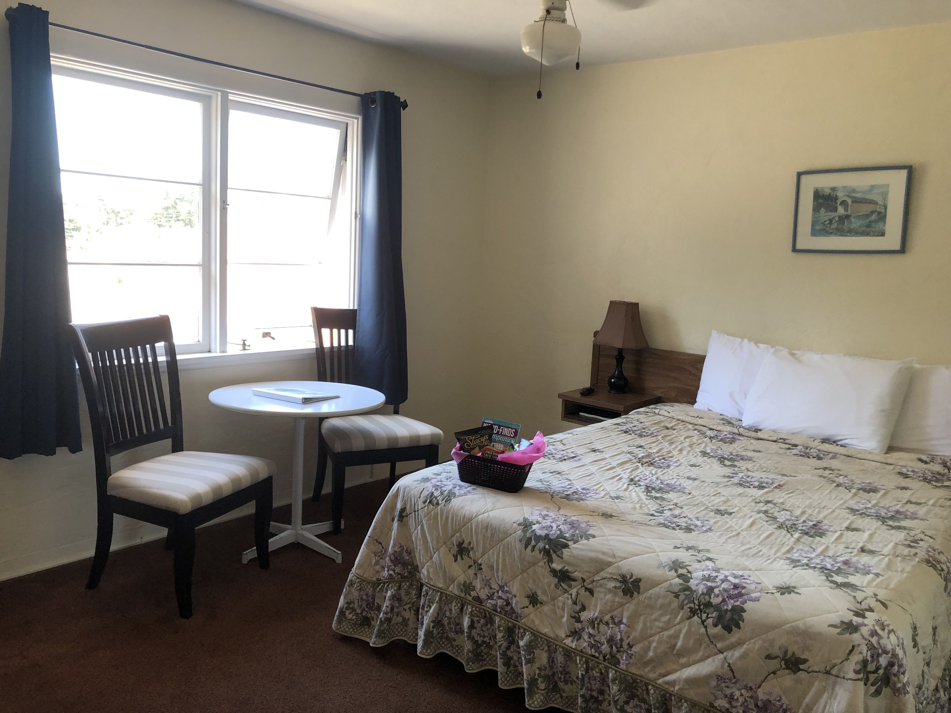 A bedroom with a bed, a chair, a small table, a lamp, and a window with curtains.