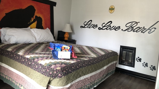 A hotel room with a large bed, a wall with the text "Live Love Bark," a wall-mounted air conditioning unit, and a nightstand with a lamp. - Florence Lighthouse Inn (Florence)