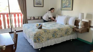 A hotel room with a bed, a nightstand, a lamp, a chair, a table, and a window with curtains.