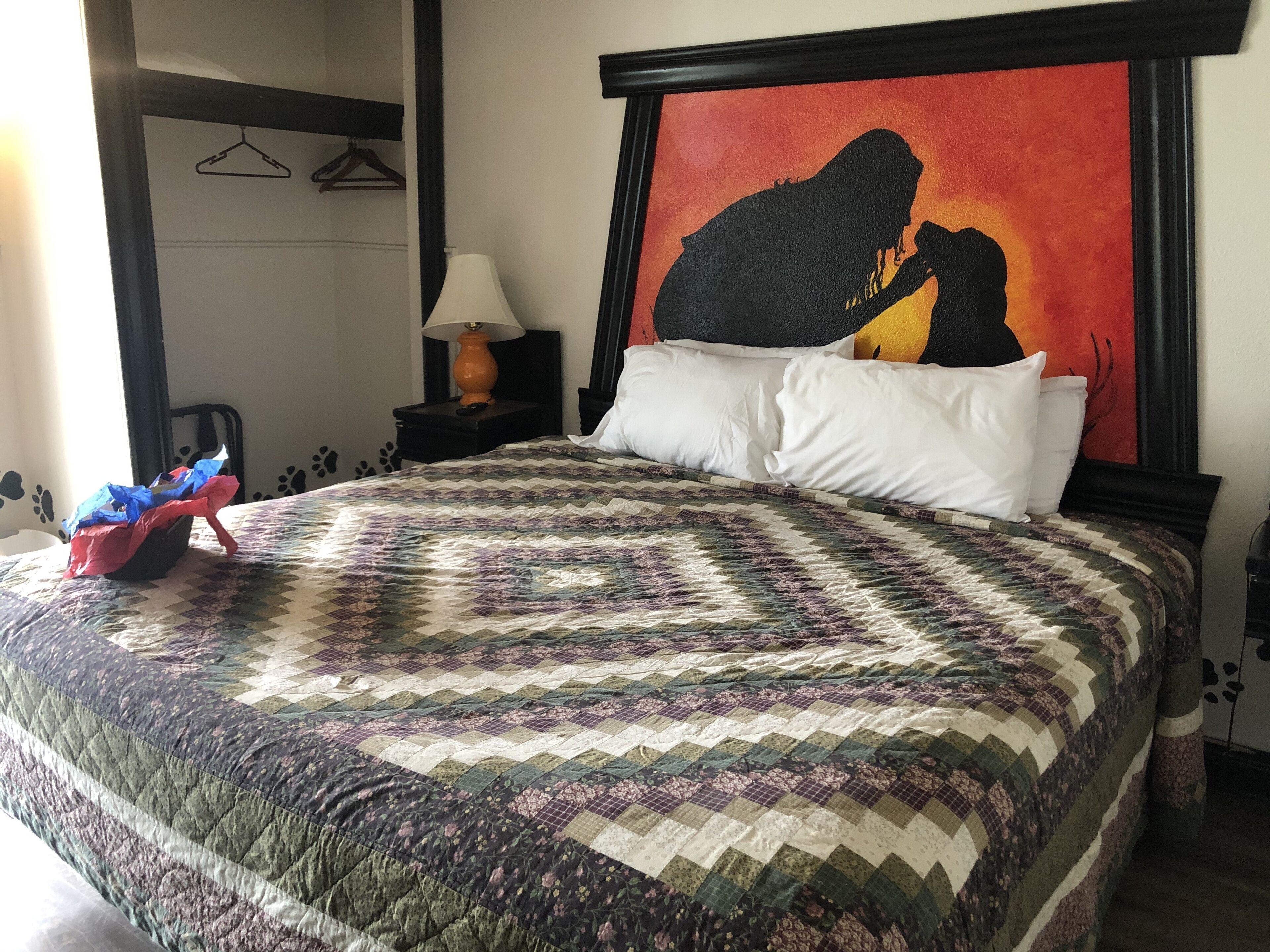 A neatly made bed with a patterned quilt, a bedside lamp, and a painting on the wall.