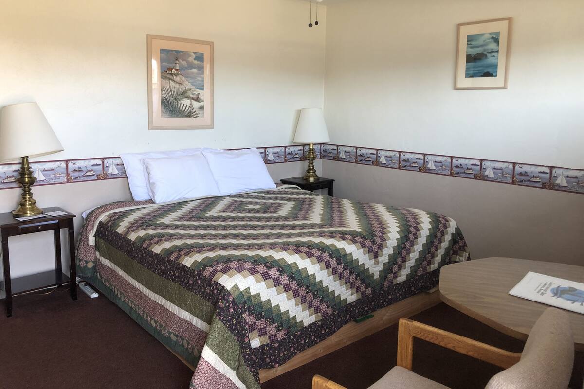A neatly arranged bedroom with a bed, two bedside tables with lamps, a small wooden table, and two chairs.
