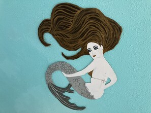 A mermaid cutout with brown hair and a grey tail against a teal background.