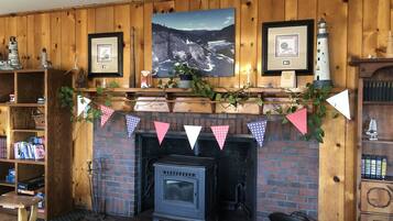 A cozy room with a fireplace, wooden walls, and a mantel decorated with framed pictures and a lighthouse model.