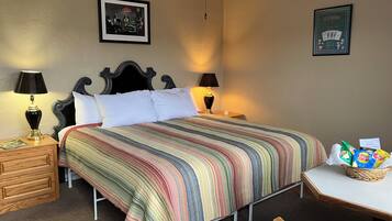 Une chambre d’hôtel avec un grand lit, deux tables de chevet, une petite table d’appoint, une petite table avec des en-cas et deux tableaux encadrés accrochés aux murs.