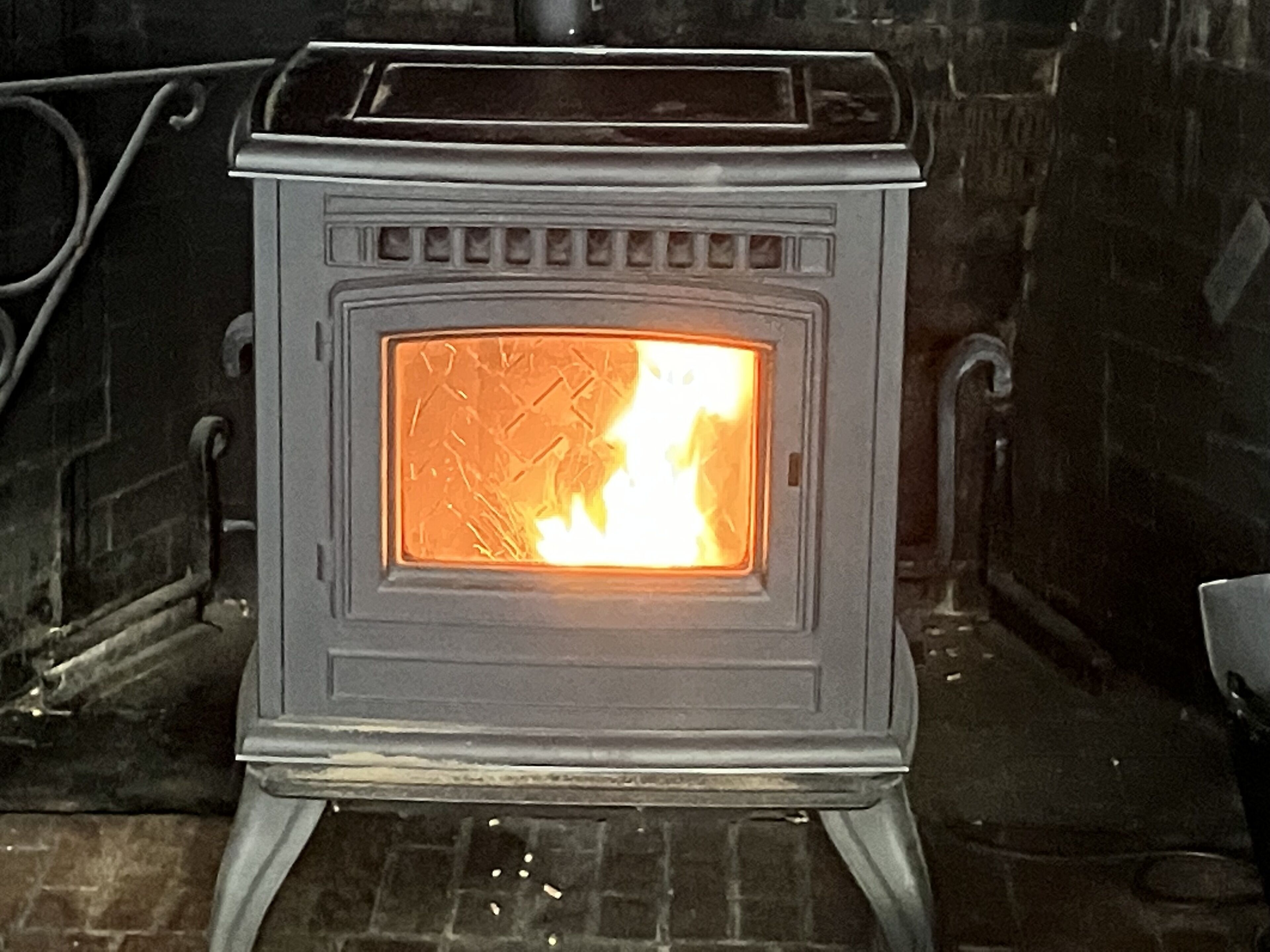A wood-burning stove with a visible fire inside, set against a brick wall.