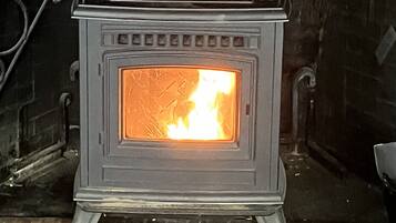 A wood-burning stove with a visible fire inside, set against a brick wall.