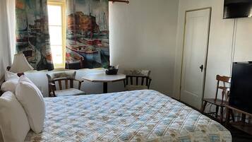 A hotel room with a bed, a small table, a chair, a TV, and a window with curtains.
