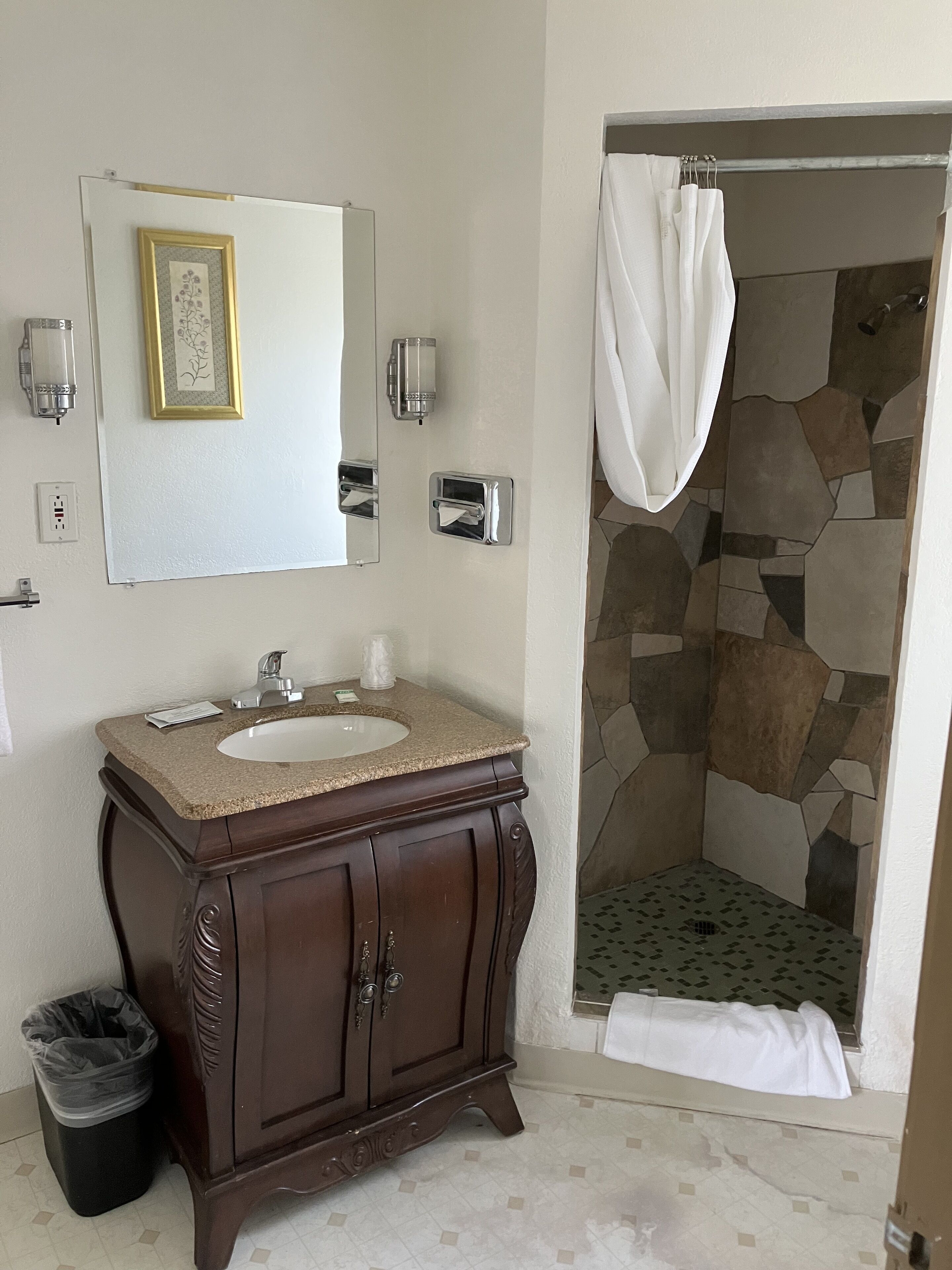 Une salle de bain avec une douche à l’italienne en pierre, un meuble-lavabo en bois et un tableau encadré au mur.