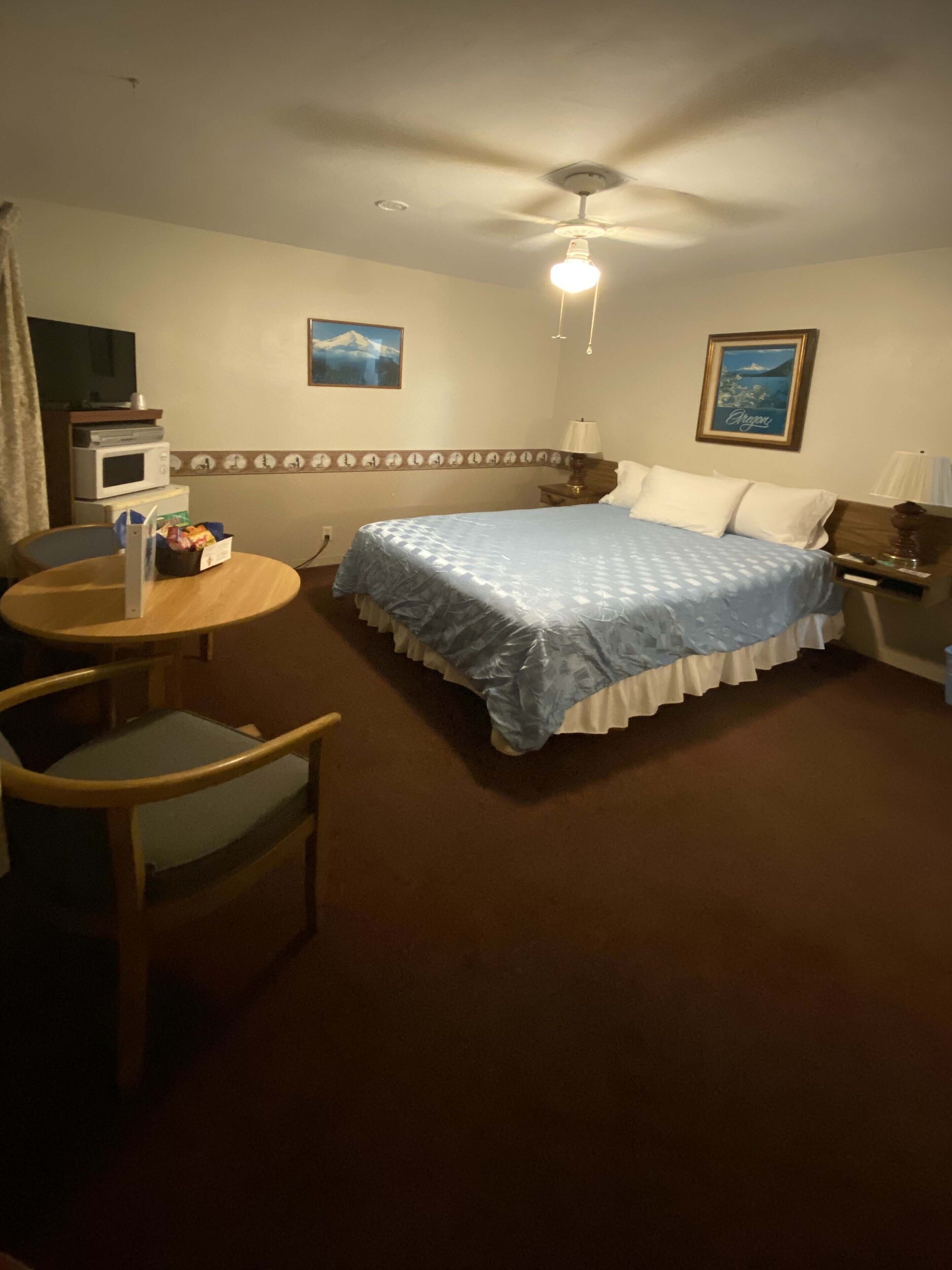 A hotel room with a bed, a desk, a chair, a microwave, and a ceiling fan.