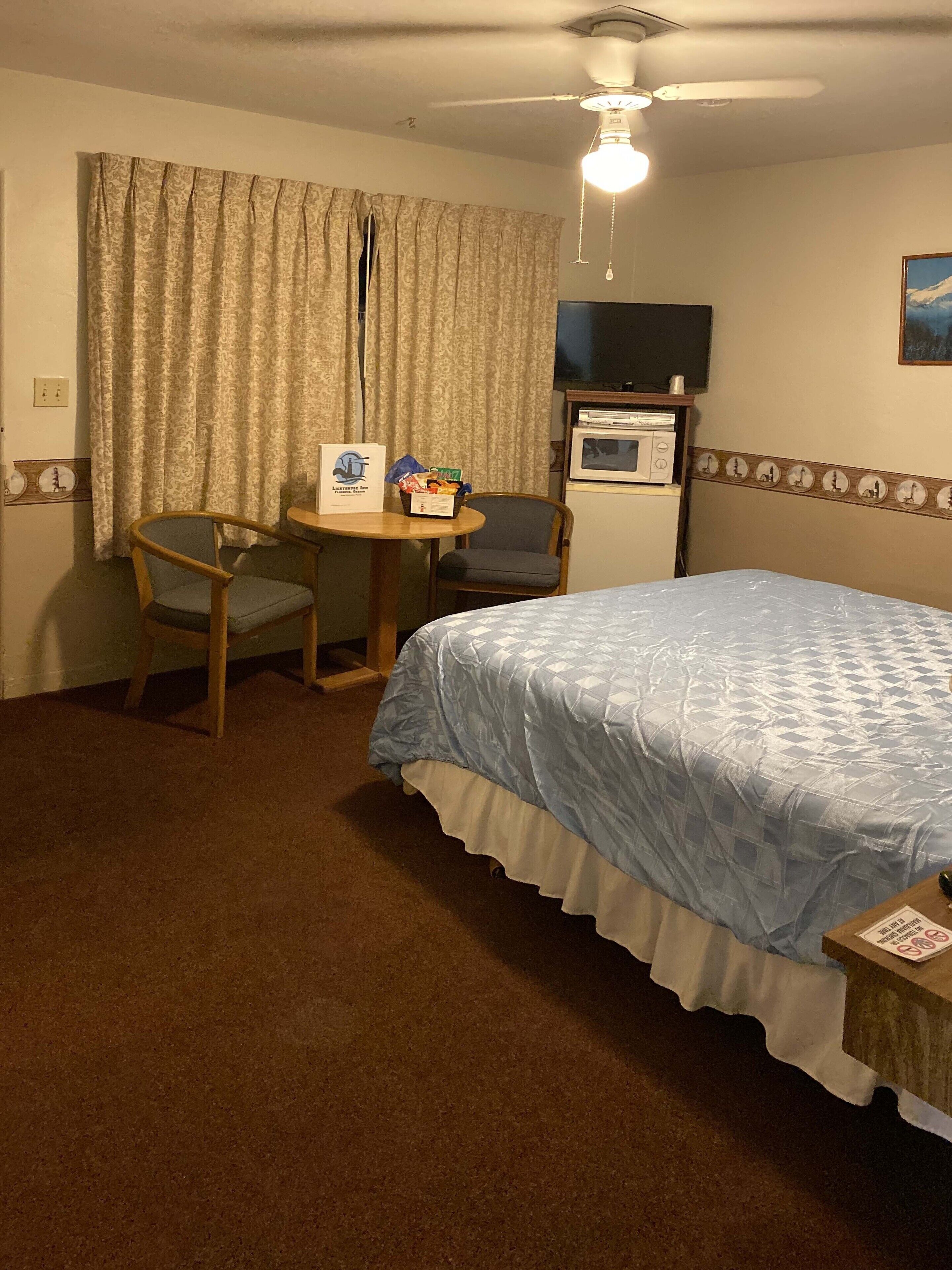 A hotel room with a bed, a small table with a chair, a television, and a microwave.