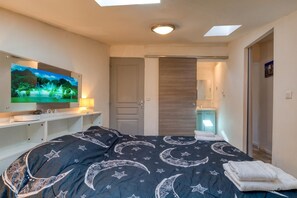 Quarto com cama, televisão, escrivaninha e banheiro visível por uma porta aberta.