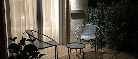 A patio with two chairs and a table, a sliding glass door, and a wall-mounted lamp.