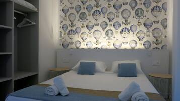 Una habitación de hotel con una cama grande, dos mesitas de noche, un armario y una pared decorada con un diseño de globos aerostáticos.