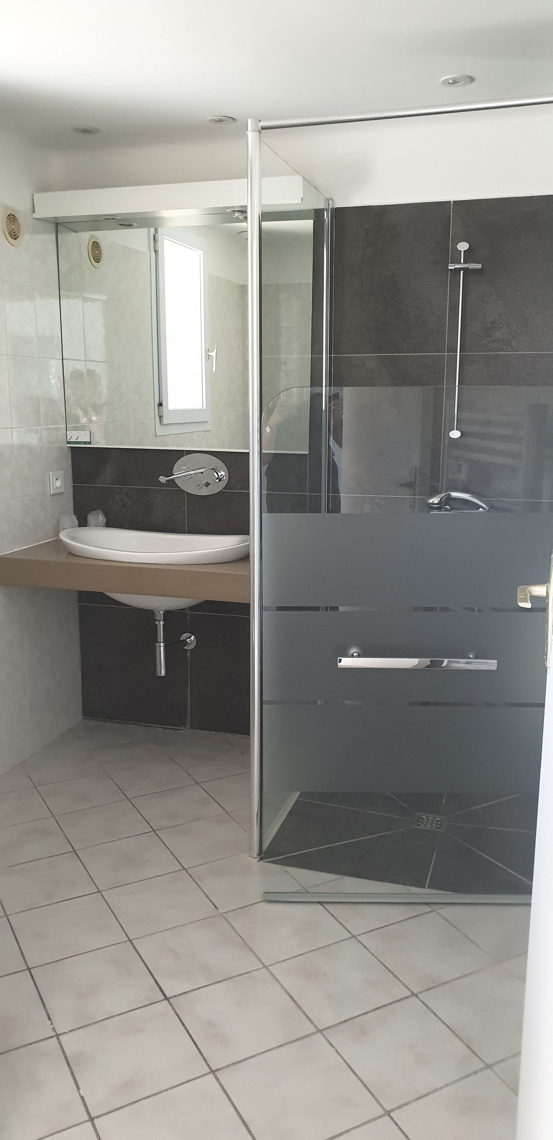 Un baño moderno con cabina de ducha de vidrio, un lavamanos con espejo y piso de baldosas.