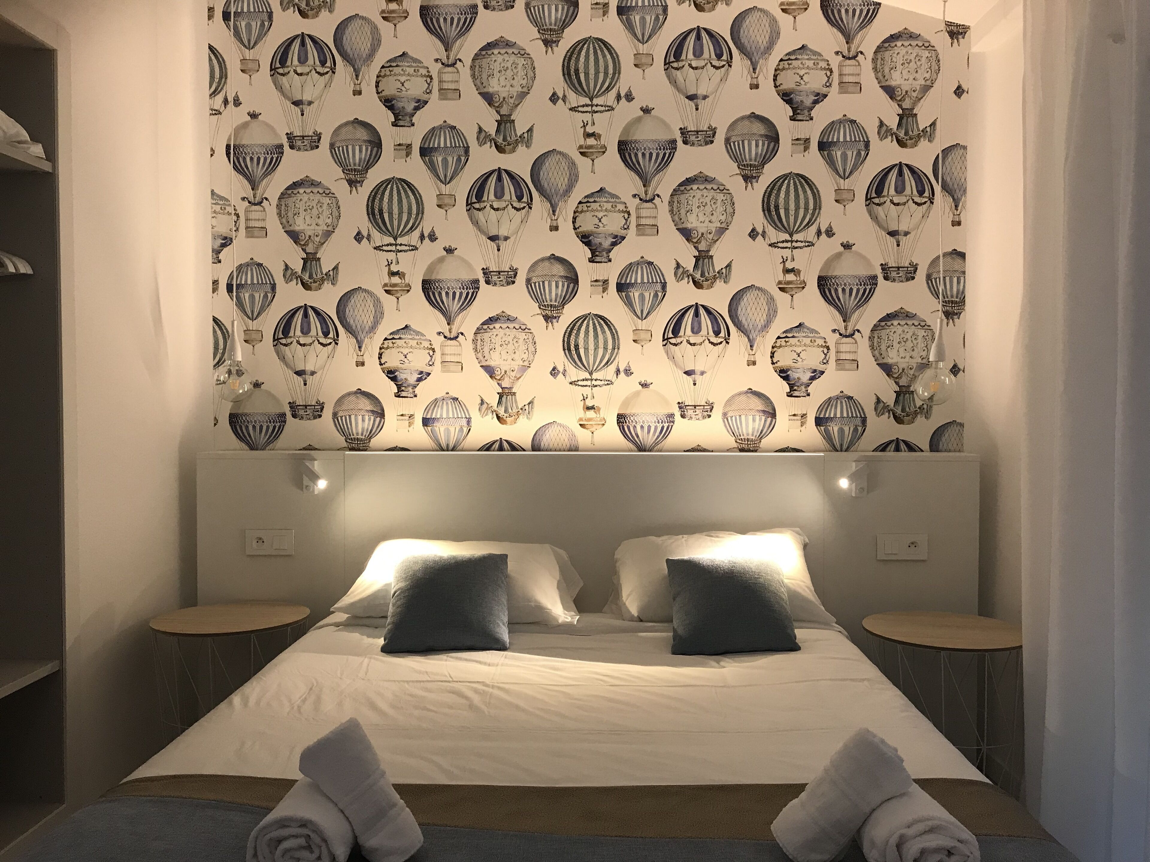 Una habitación de hotel con una cama grande, dos mesitas de noche y una pared decorada con un diseño de globos aerostáticos.