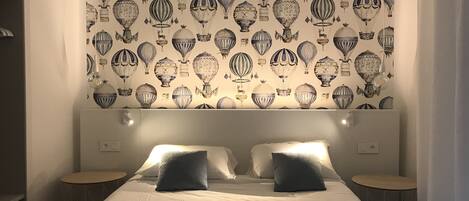 A hotel room with a large bed, two bedside tables, and a wall with a pattern of hot air balloons.