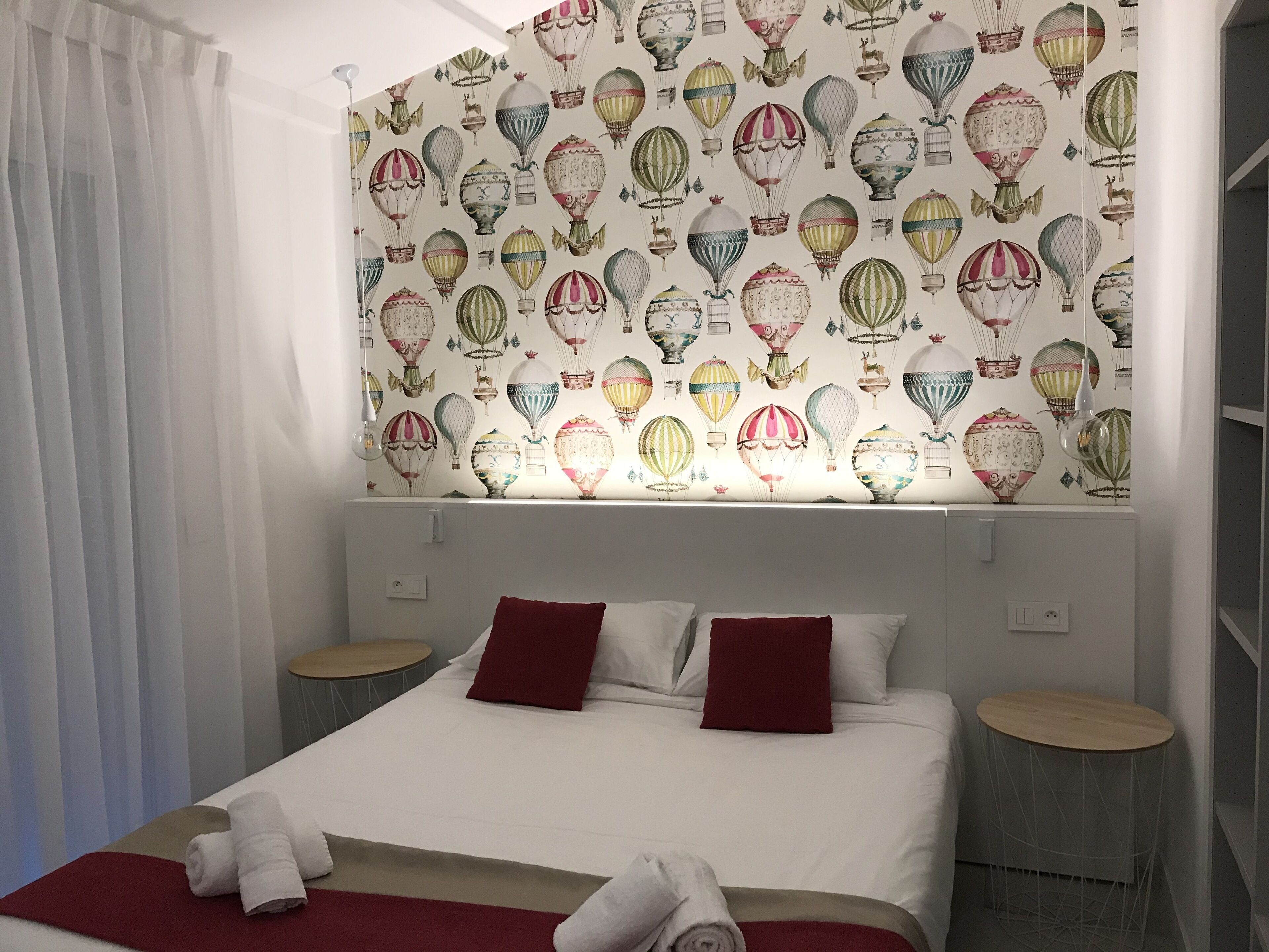 A hotel room with a large bed, two bedside tables, and a wall decorated with a pattern of hot air balloons.