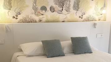 Un letto ben rifatto con copriletto bianco e marrone, due cuscini e un asciugamano arrotolato.