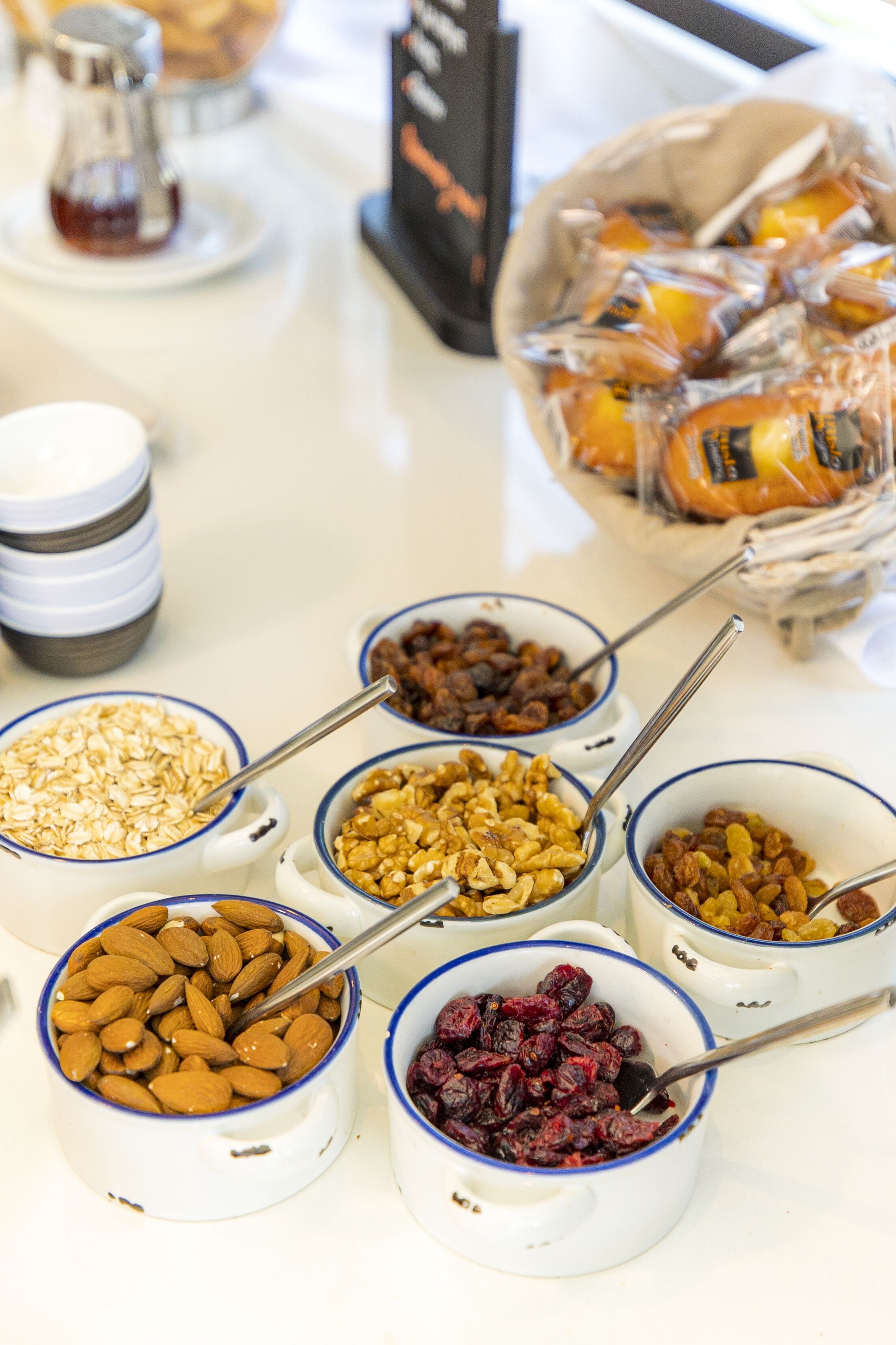 Un bufé de desayuno con diversos alimentos en cuencos, como avena, almendras, nueces y frutas secas.