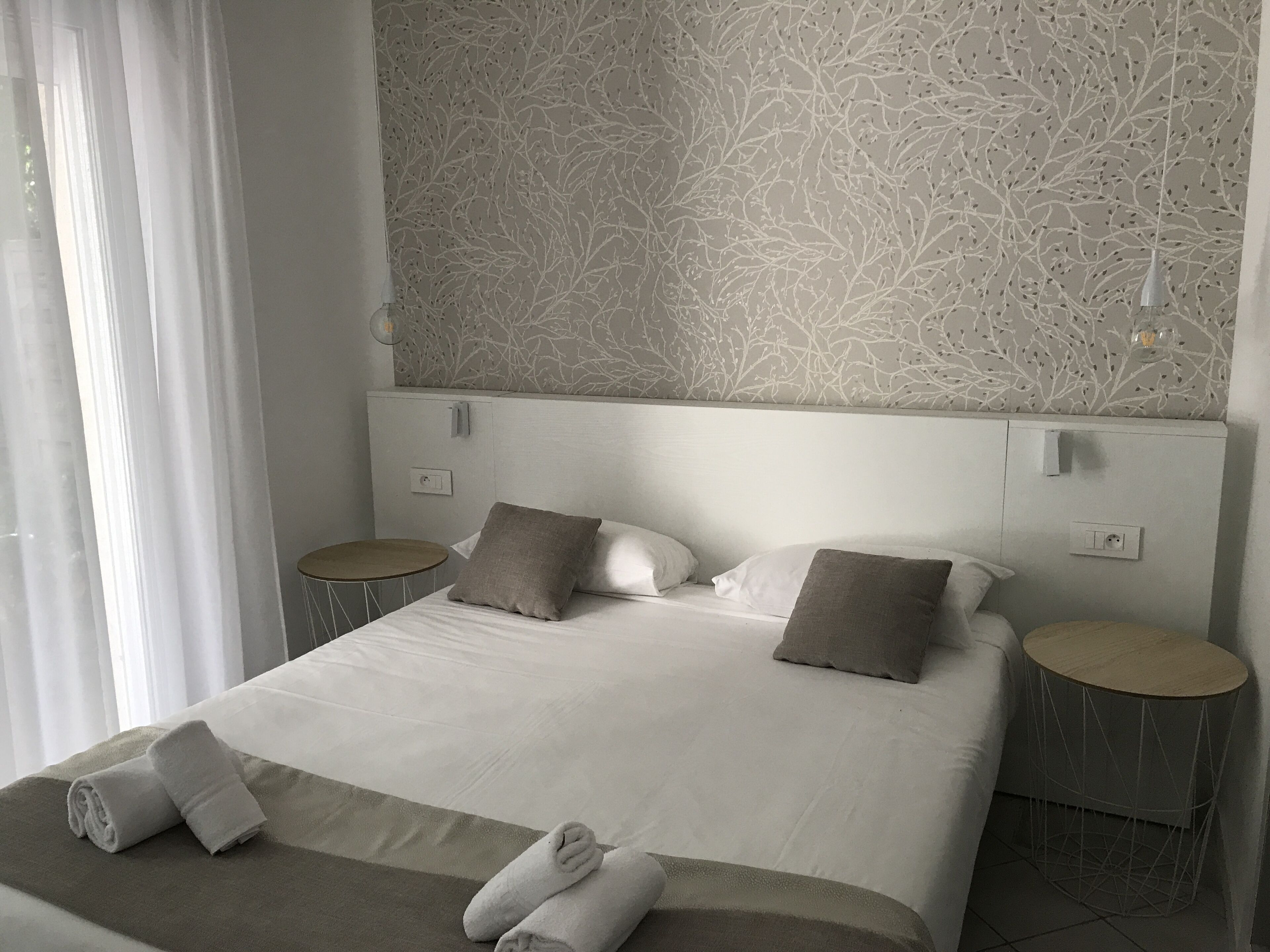 Una cama bien hecha con almohadas y toallas, una mesita redonda y una pared con un estampado de ramas de árbol.