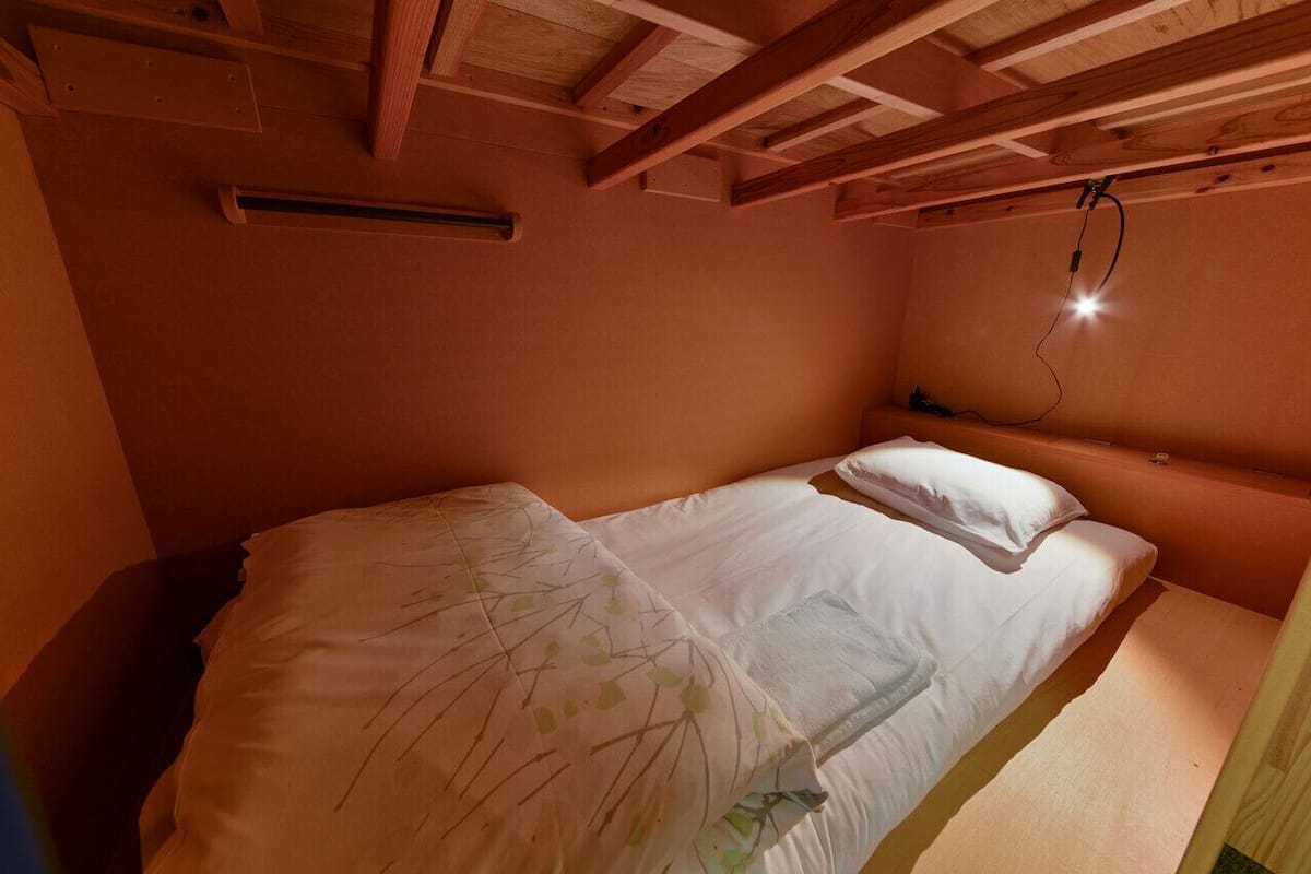 A single bed with white bedding in a room with wooden beams on the ceiling and a wall-mounted light fixture.
