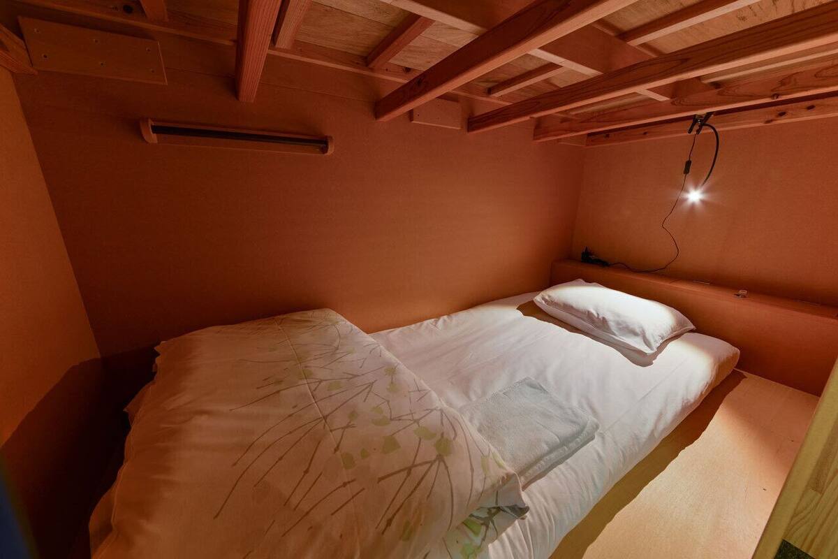 A single bed with white linens, a wooden ceiling, and a wall-mounted light fixture.