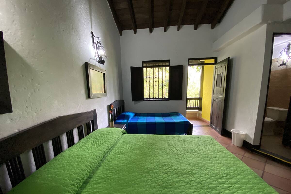 A room with two beds, a window with bars, a door leading outside, and a wall-mounted light fixture.