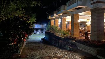 A nighttime view of a courtyard with a stone pathway leading to a building with a brick facade and outdoor seating area.