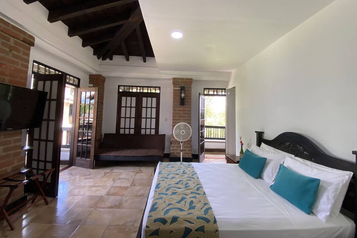 A hotel room with a bed, a fan, a bench, and a TV.
