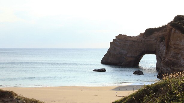 A coastal landscape with a natural rock arch formation, sandy beach, and calm sea. - Tanegashima Minshuku Yu-yu (Minamitane)