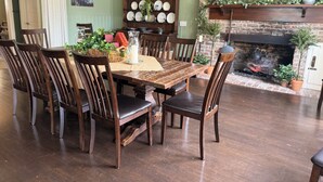 Een eethoek met een houten tafel en stoelen, een open haard van baksteen, en een wand versierd met borden en een schilderij.