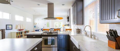 A modern kitchen with a central island, stainless steel appliances, and a large window with blinds.
