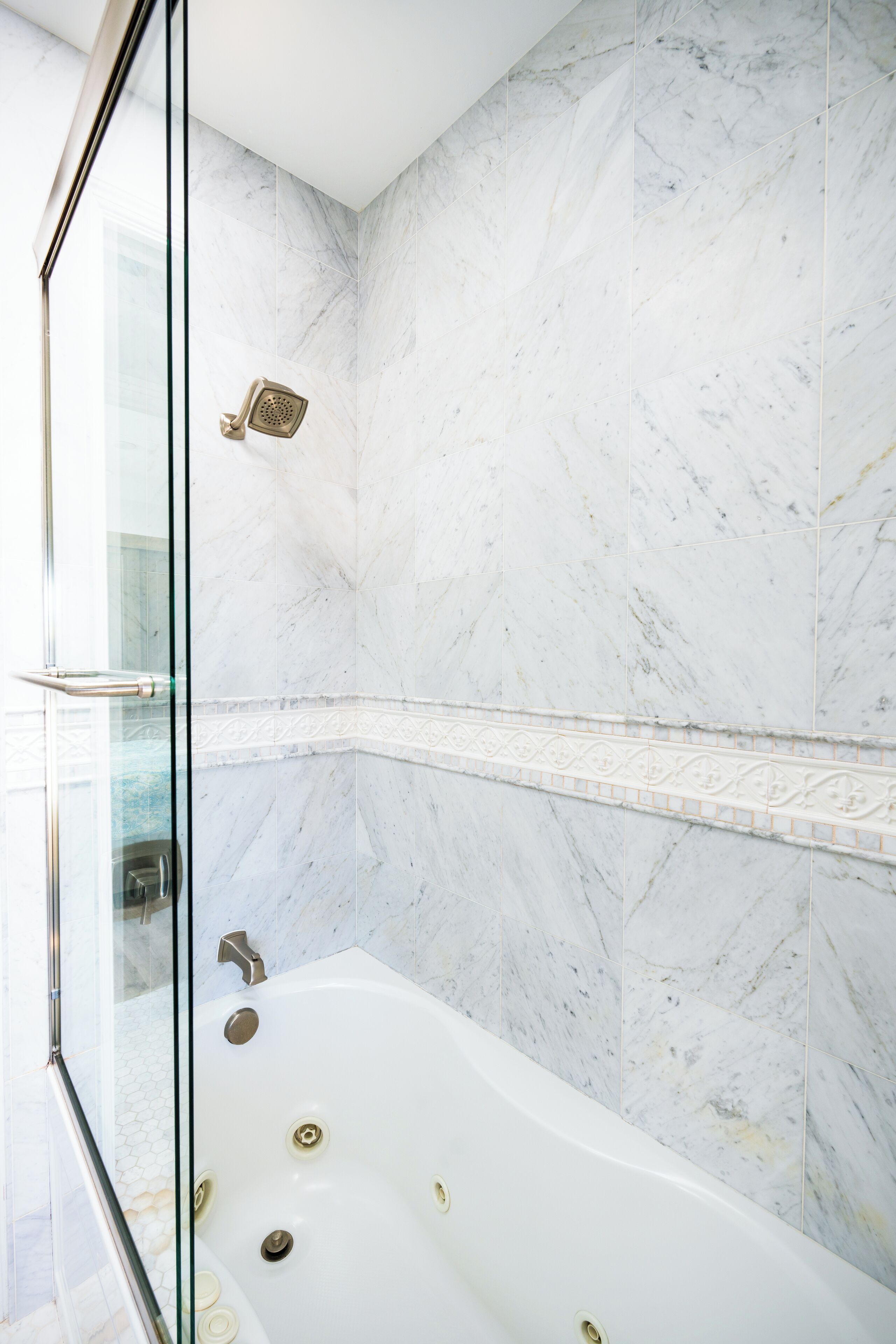 A modern bathroom with a glass-enclosed shower, a freestanding bathtub, and marble walls.