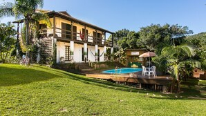 A two-story house with a swimming pool, surrounded by a lush garden and palm trees. - Guarda Beach House - Hostel (Palhoça)