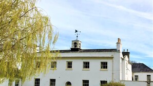 A white building with a central entrance, multiple windows, and a weather vane on the roof. - Beachborough Park (Folkestone)