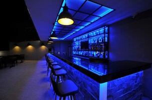 Una zona de bar con una barra larga, taburetes y un estante con botellas.