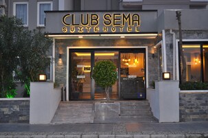 Entrada del Club Sema Suite Hotel, con fachada de piedra, puertas de vidrio y un pequeño árbol en el centro.