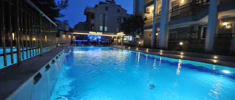 A swimming pool at dusk with a bar and restaurant in the background.