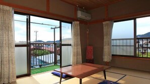 A tatami mat room with a low table, sliding glass doors, and a view of a green landscape. - Minshuku Urashima (Minamiizu)