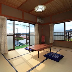 Una habitación con esteras tatami, una mesa baja, puertas correderas de vidrio y vistas a un paisaje verde.