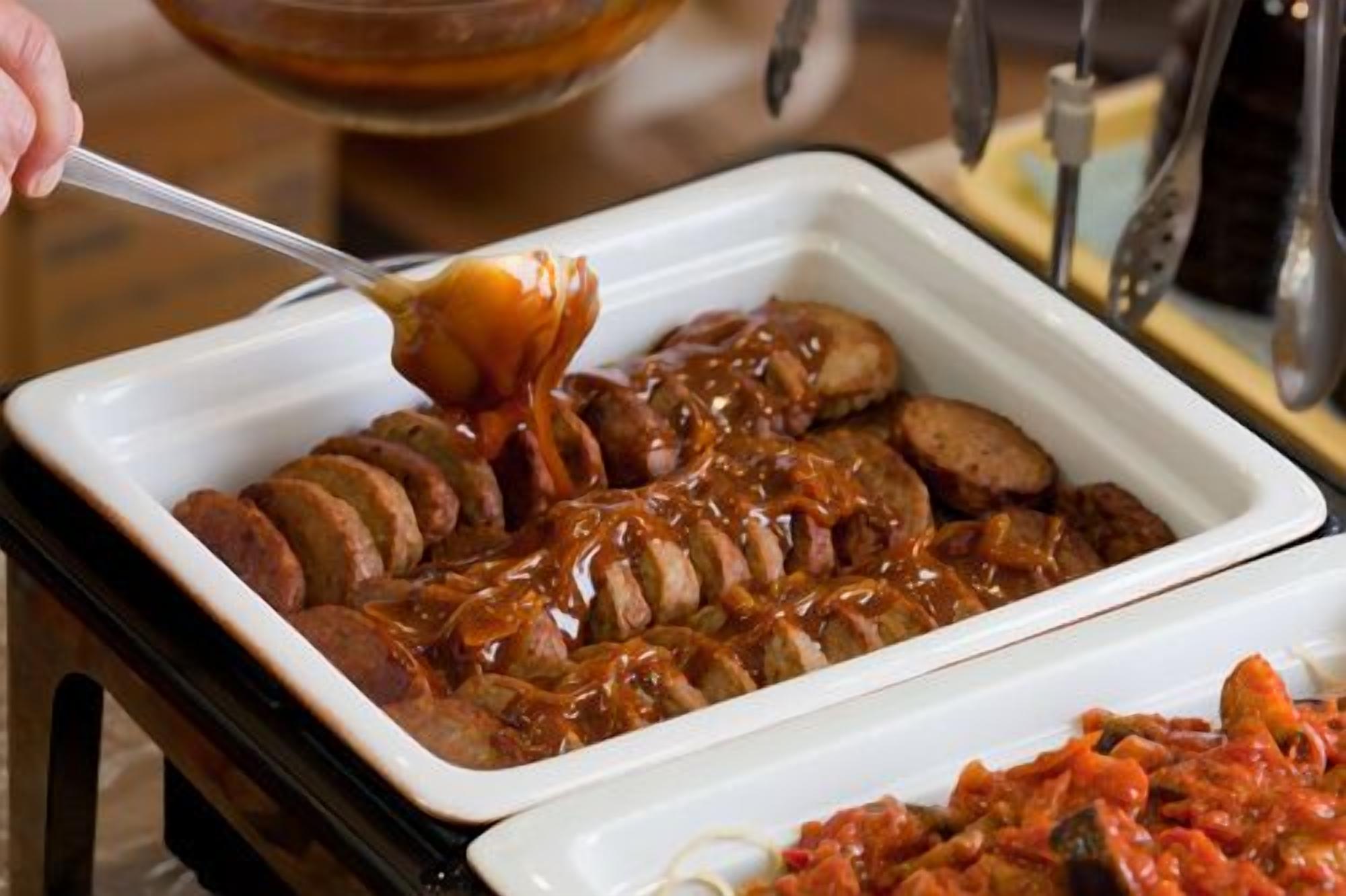 A white rectangular dish with sliced meat covered in sauce, a spoonful being lifted, and a smaller dish with red sauce in the foreground.