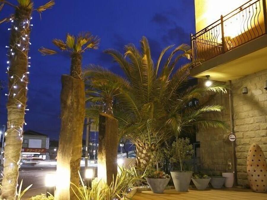 Un edificio con fachada de piedra, un balcón con barandilla de hierro forjado y plantas en macetas.